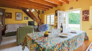A dining area with a table set for four, a staircase, and a sofa in a room with wooden beams and yellow walls.