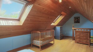 A room with a sloped ceiling, a crib, a dresser, and a window.