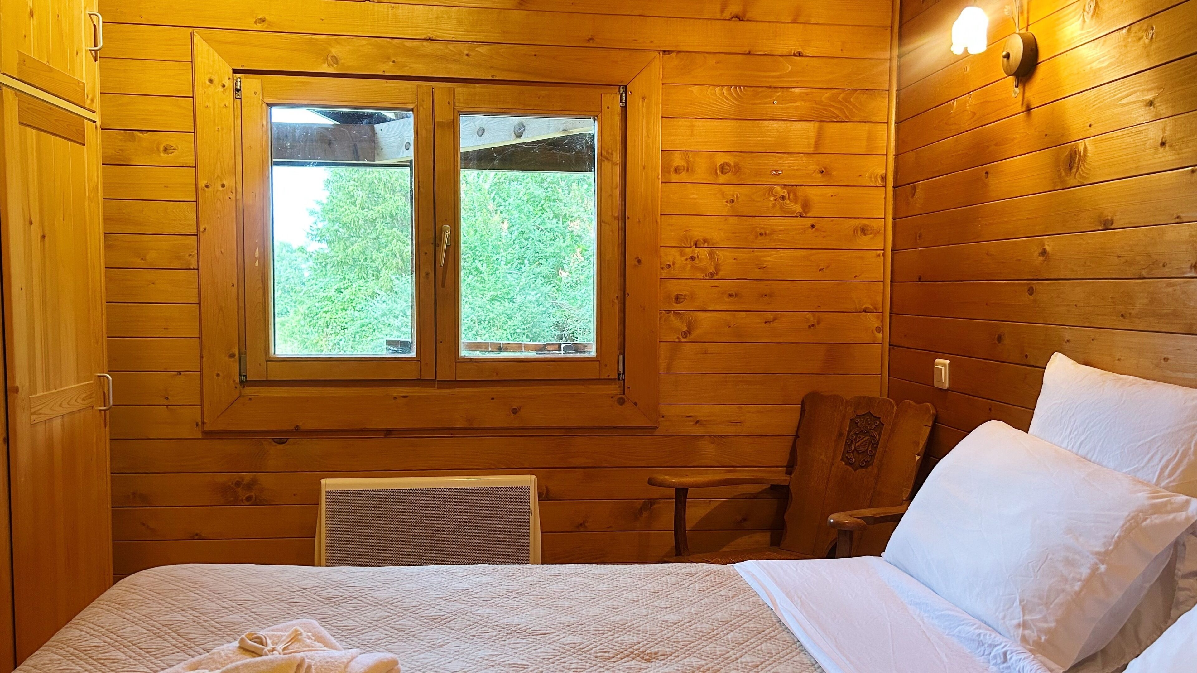 A wooden cabin room with a bed, a window, and a chair.
