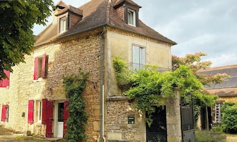 A stone building with red shutters, a balcony, and ivy growth.