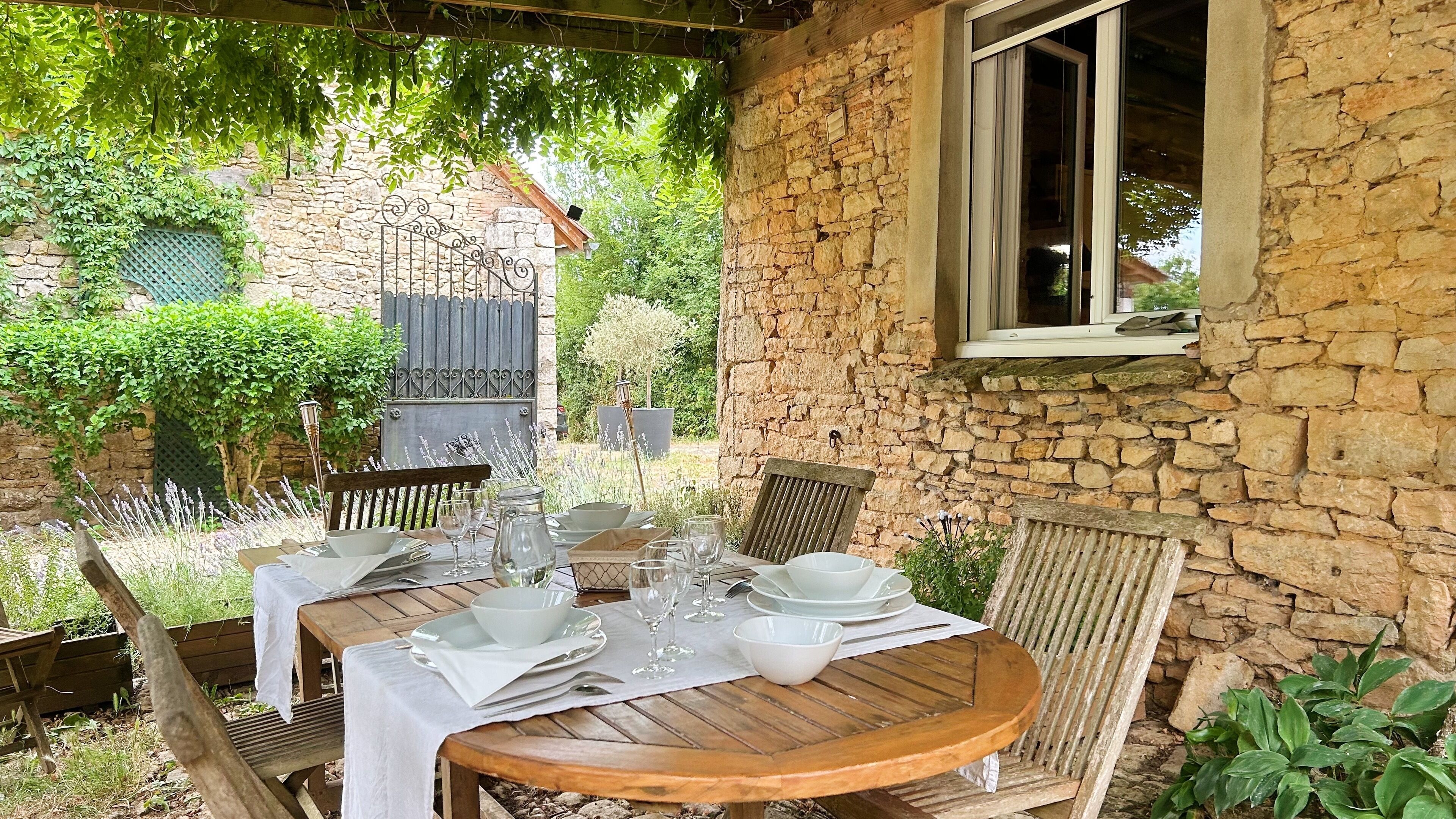 An outdoor dining area with a stone wall, wooden table, and chairs.