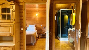 A wooden cabin interior with a bed, a chair, and a kitchenette.