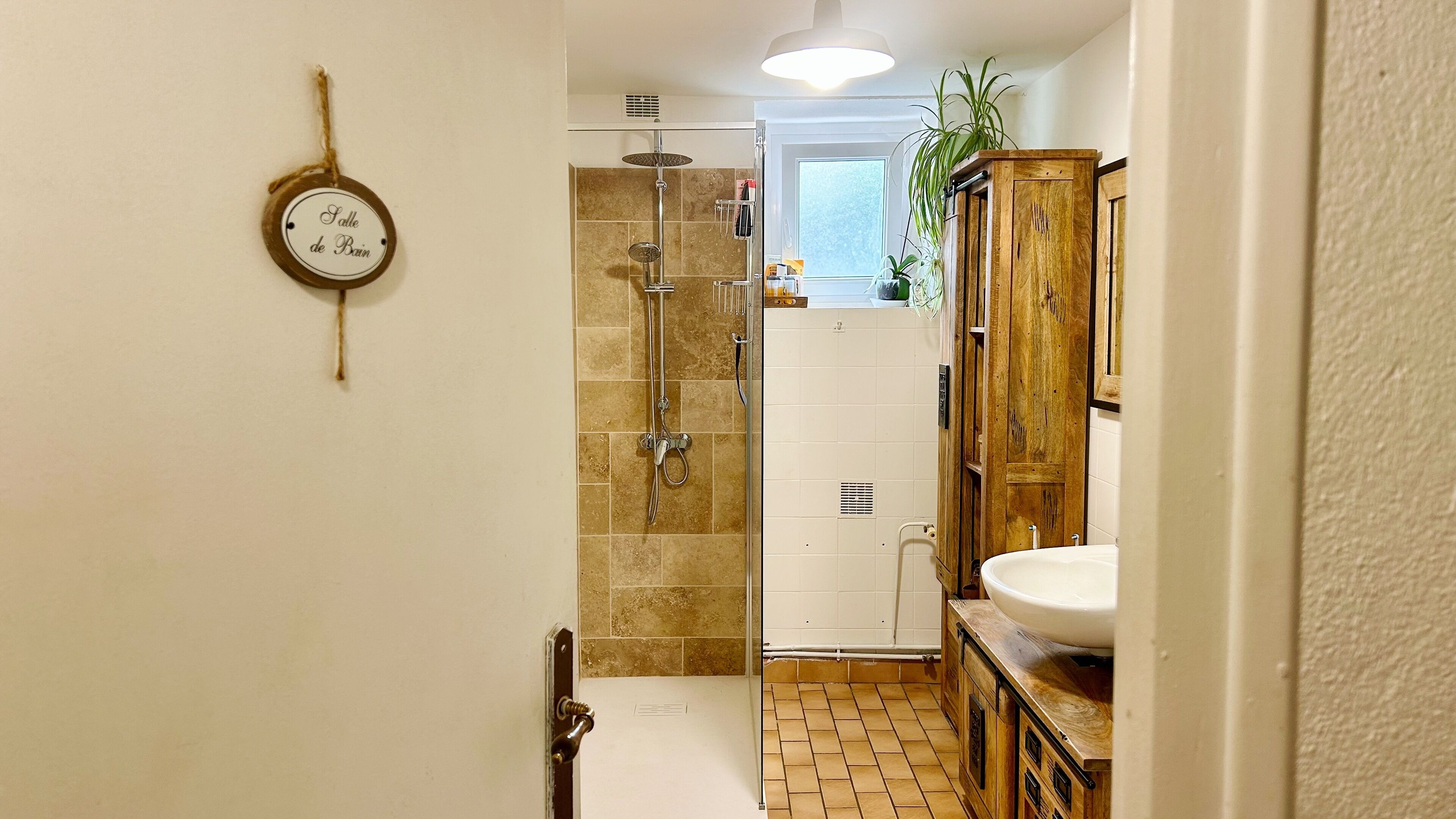 A bathroom with a shower, a sink, and a wooden cabinet.