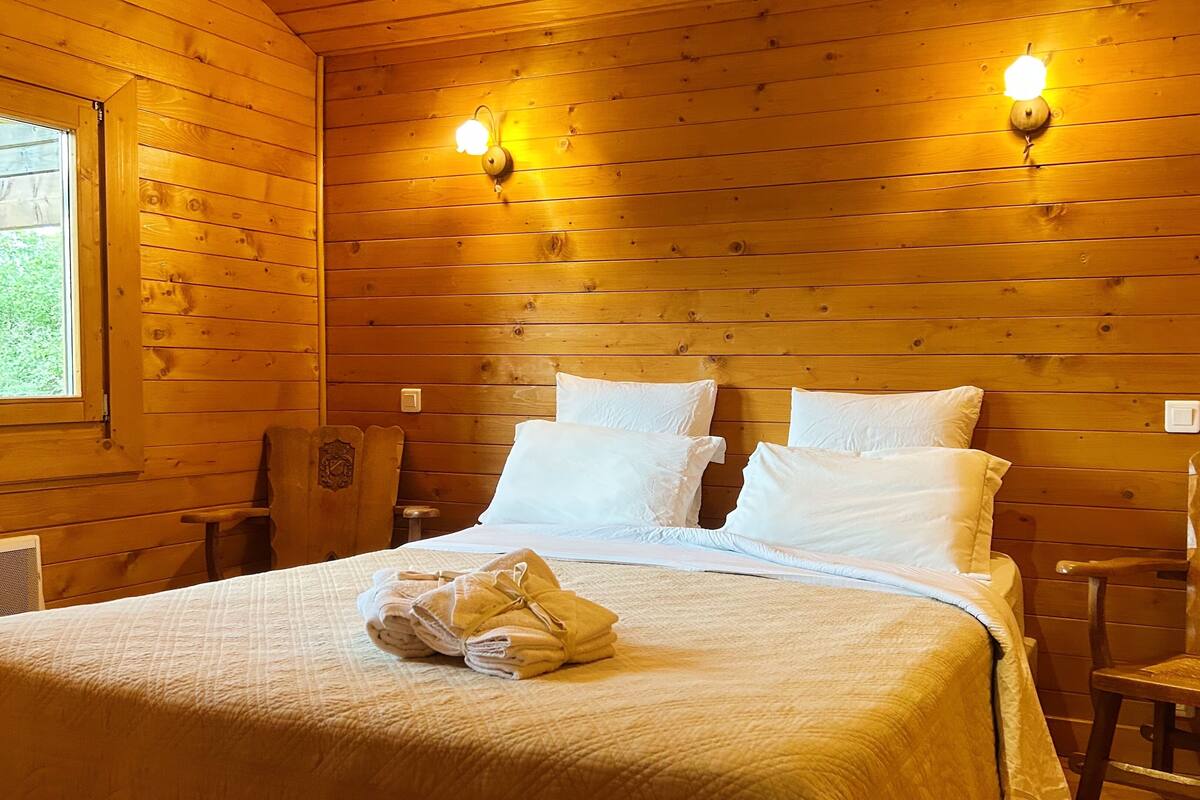 Une pièce de cabane en bois comprenant un lit, deux chaises et deux lampes fixées au mur.