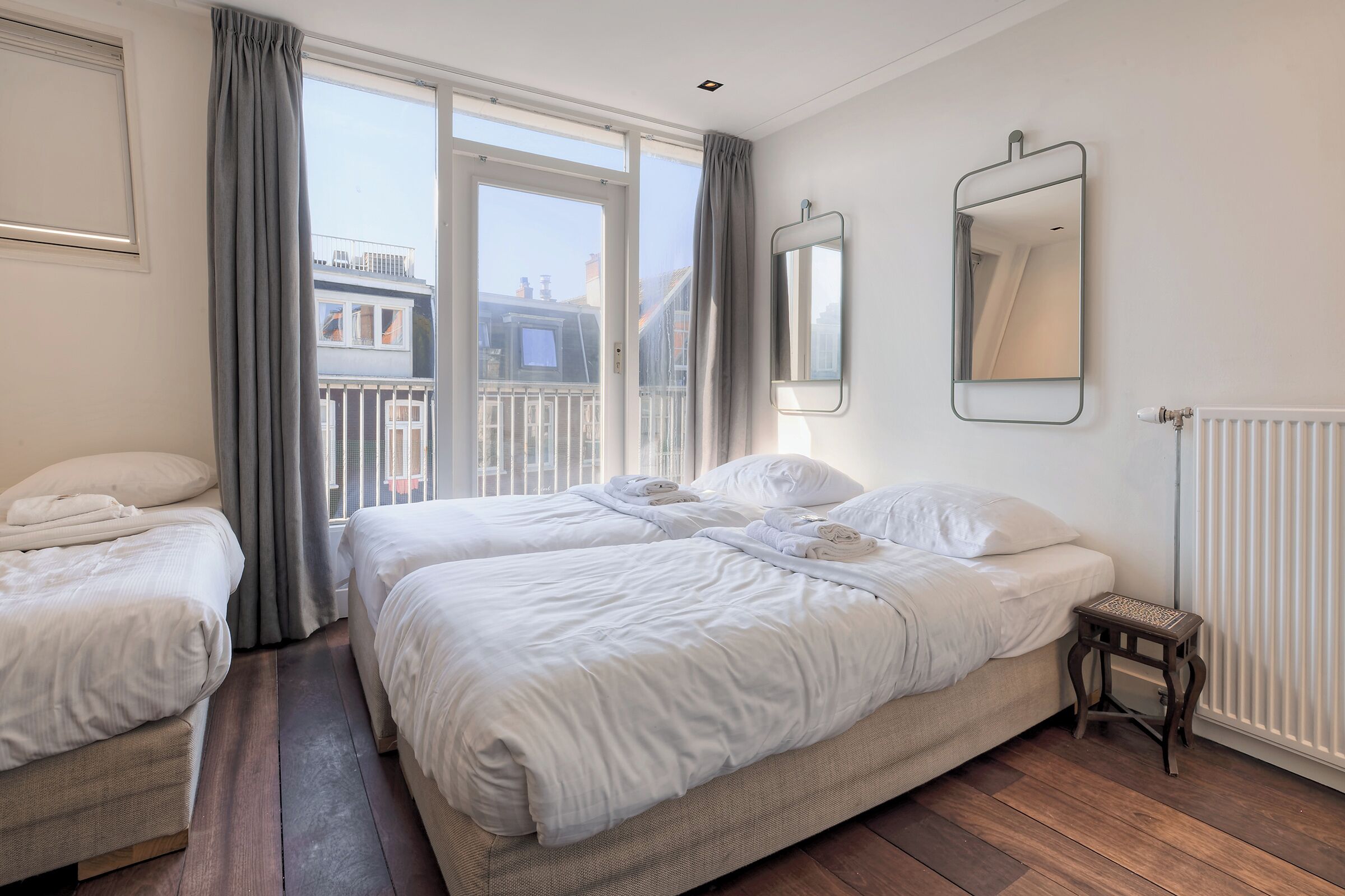 Ett hotellrum med två sängar, ett fönster med gardiner, ett element och en liten träpall.