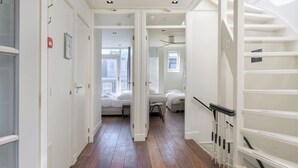 Un couloir doté d’un plancher en bois, de murs blancs et d’un escalier avec une main courante noire.