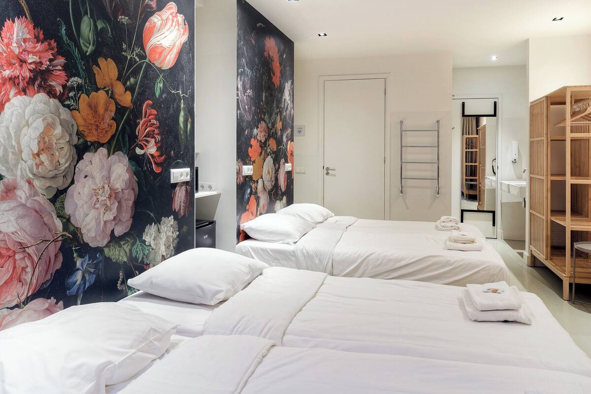 Hotelkamer met twee bedden, een groot bloemenwanddecor, een houten kledingkast en een badkamer met een handdoekhouder.