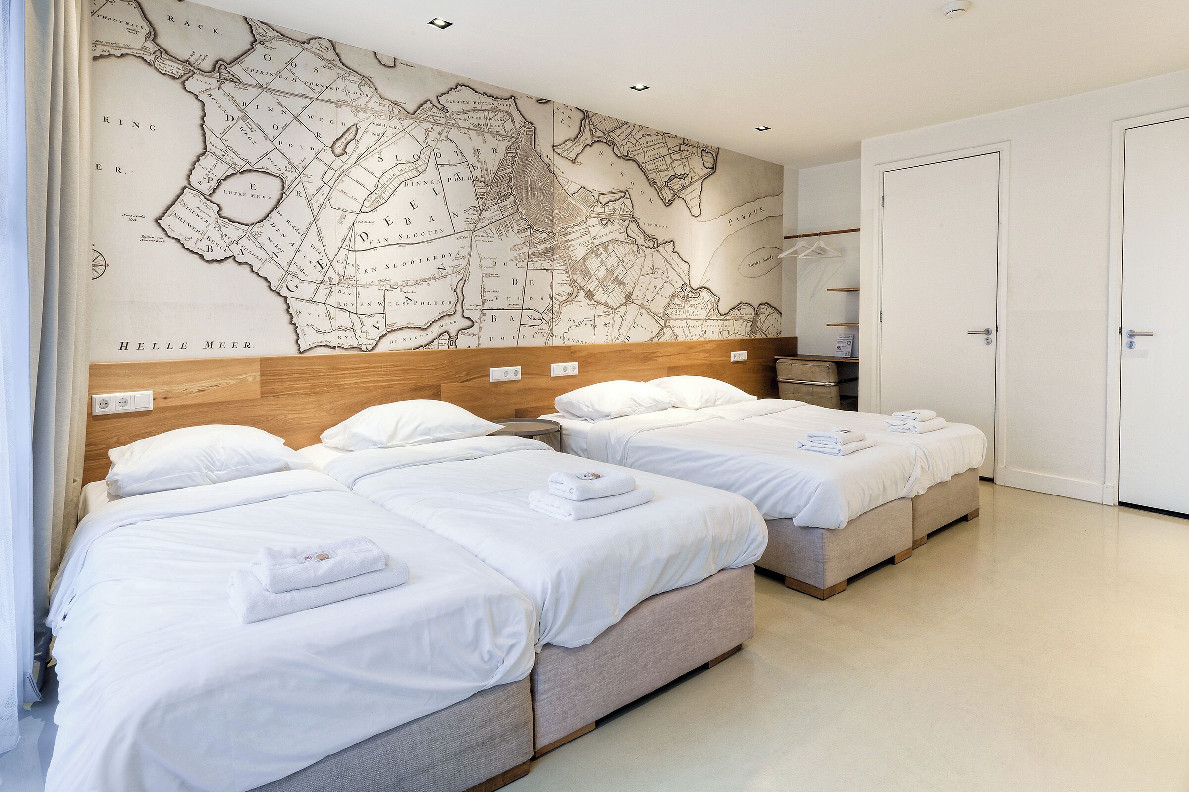 A hotel room with two beds, a large map on the wall, and a wardrobe.