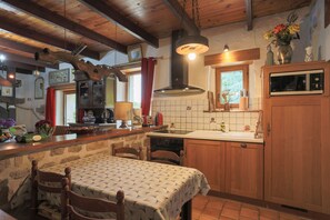 A rustic kitchen with wooden beams, a stone wall, a tiled backsplash, a wooden dining table, and a built-in oven.