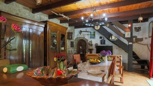 A rustic dining area with wooden furniture, a chandelier, stone walls, and a staircase. - Holiday Home 'Ty Coz' with Private Terrace, Private Garden and Wi-Fi (Lanvellec)
