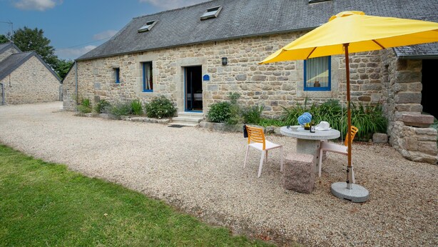 A stone building with a gravel driveway, a yellow umbrella, a table with chairs, and a small garden area. - Holiday Home 'Ty Coz' with Private Terrace, Private Garden and Wi-Fi (Lanvellec)