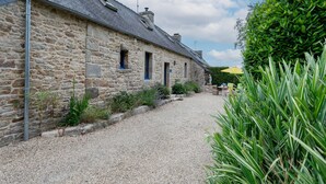 A stone building with a gravel driveway, a small garden, and a yellow umbrella. - Holiday Home 'Ty Coz' with Private Terrace, Private Garden and Wi-Fi (Lanvellec)