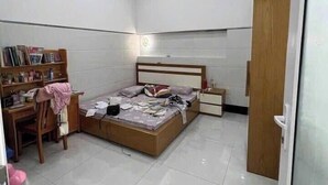 A bedroom with a bed, a desk, a chair, a bookshelf, and a blue trash bin. - Imperia Sky Garden Dream Loft (Hanoi)