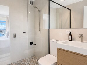 A modern bathroom with a glass-enclosed shower, a white sink with a wooden cabinet, and a large mirror. - Amazing location on Fisherman’s Wharf only minutes to vibrant Fremantle nightlife and cafes. Enjoy the infamous West Australian Sunsets on your private balcony. (Fremantle)