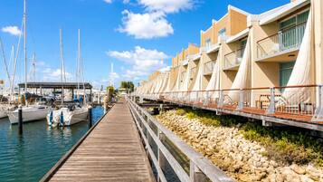 A marina with boats docked, a wooden pier leading to a row of buildings with balconies.