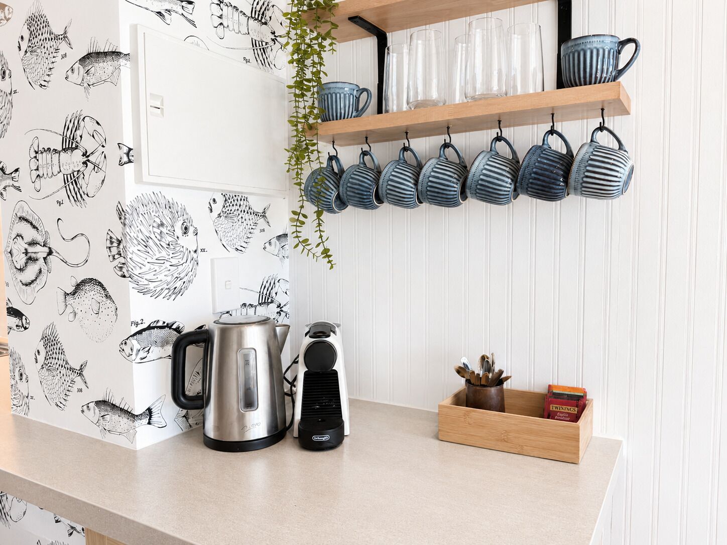 A kitchen with a kettle, coffee maker, and a wooden box with kitchen utensils.
