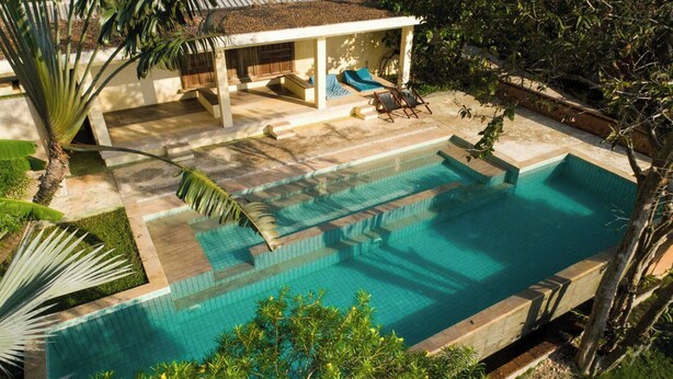 Une piscine avec des marches permettant d’y accéder, entourée d’un patio couvert aménagé avec des sièges.