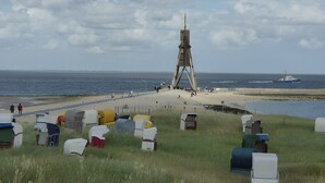 Una playa con una gran estructura de madera, un sendero arenoso y varias tiendas de colores.