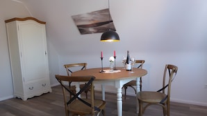 Un comedor con una mesa redonda, cuatro sillas, una lámpara colgante, un armario blanco y un cuadro en la pared.