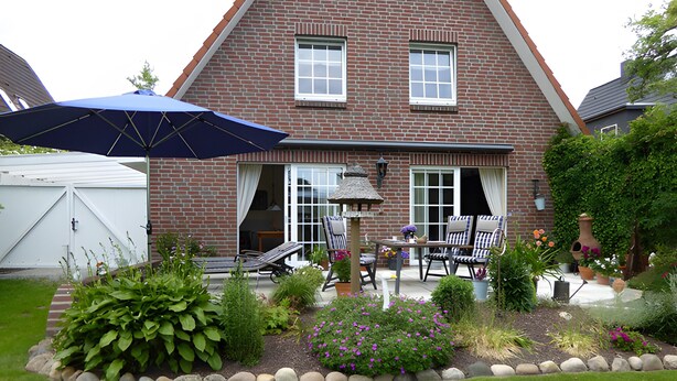 Una casa de ladrillo con patio, mobiliario exterior y jardín.