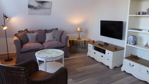 Una sala de estar con un sofá, una mesa de centro, un televisor, una estantería y una maleta.