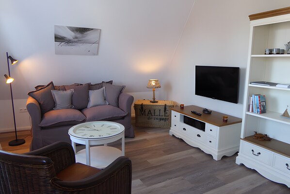 A living room with a sofa, a coffee table, a TV, a bookshelf, and a suitcase.