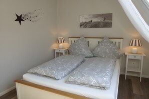 A bedroom with a bed, two nightstands, a star wall decoration, a landscape painting, and a slanted ceiling.