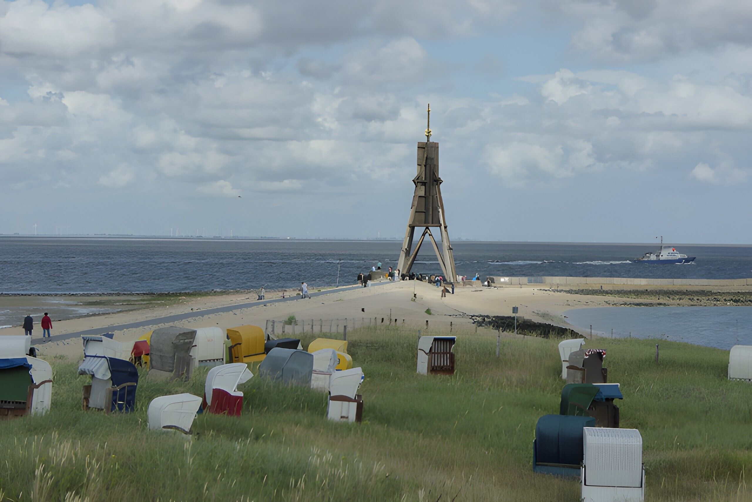 A beach with a large wooden structure, a sandy path, and several colorful tents.