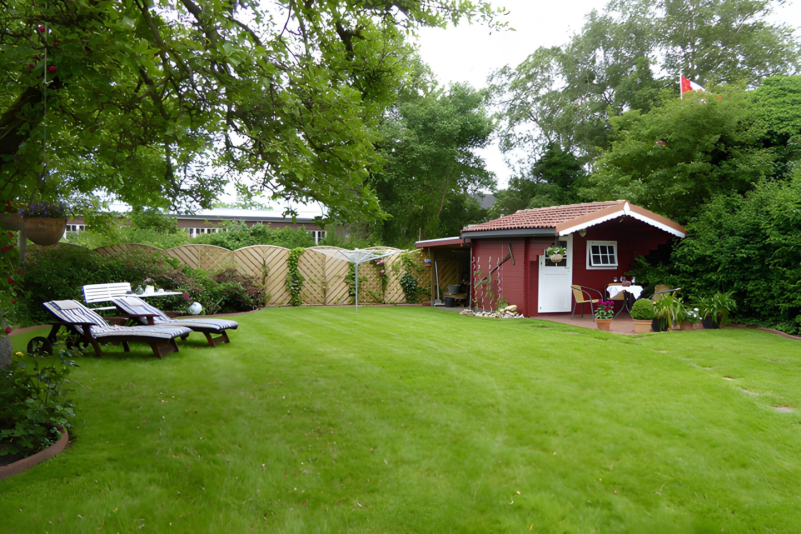 A red building with a white door, a small patio with a table and chairs, and a well-maintained lawn.
