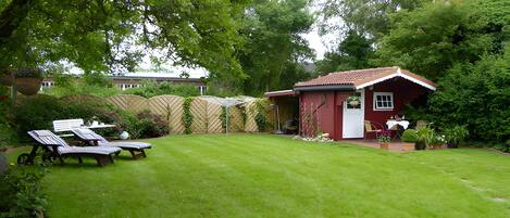 A red building with a white door, a small patio with a table and chairs, and a well-maintained lawn.