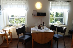 Un coin repas avec une table dressée pour deux personnes, deux verres à vin, deux bougies et une petite plante en pot.