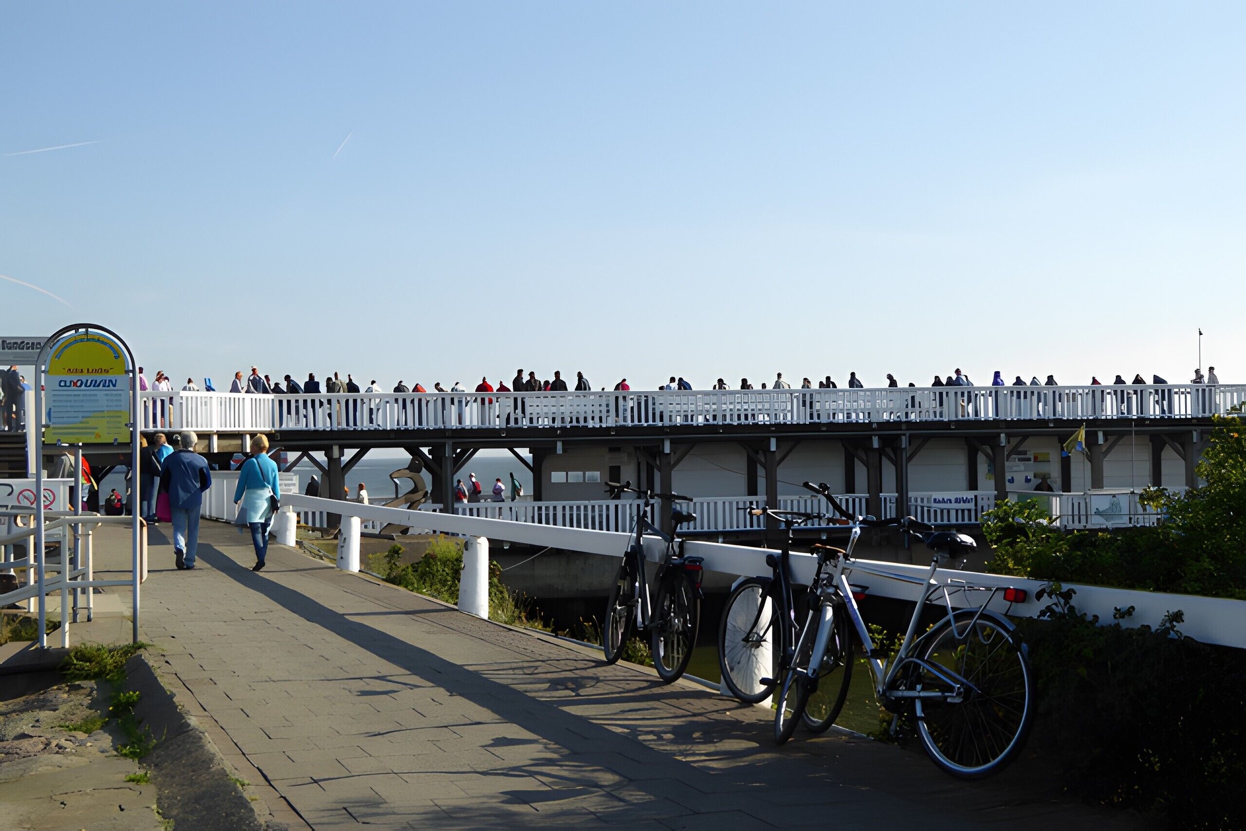 A pedestrian bridge with a white railing, bicycles parked, and a sign on the left.