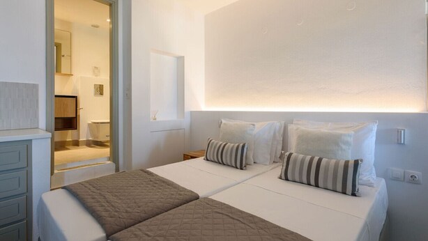 A modern bedroom with a bed, bedside tables, and a walk-in closet. - Phaedrus Living: Paros Cycladic Residences 2 (Piso Livadi)
