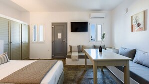 A hotel room with a bed, a sofa, a table, and a TV. - Phaedrus Living: Paros Cycladic Residences 2 (Piso Livadi)