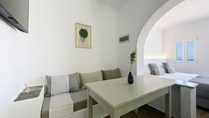 A minimalist room with a white sofa, a small table, and a bed with a view of the sea.