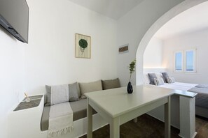 Une pièce au décor minimaliste, avec un canapé blanc, une petite table et un lit donnant sur la mer.