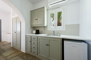 A compact kitchen with a built-in dishwasher, a window with a view of palm trees, and a white countertop. - Phaedrus Living: Paros Cycladic Residences 4 (Piso Livadi)