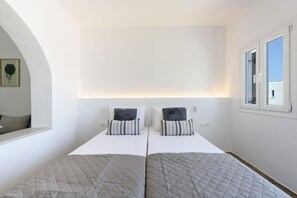 A bedroom with two beds, a large window, and a wall-mounted light fixture. - Phaedrus Living: Paros Cycladic Residences 4 (Piso Livadi)