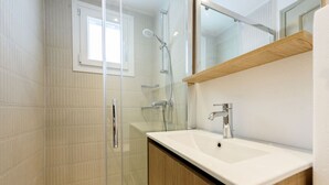 A modern bathroom with a glass shower enclosure, a white sink, and a wooden vanity.