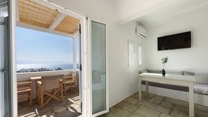 A balcony with a view of the sea, a seating area with a table, and a flat-screen TV mounted on the wall. - Phaedrus Living: Paros Cycladic Residences 6 (Piso Livadi)