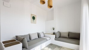 A modern, minimalist living room with a grey sofa, a small side table, and a woven light fixture. - Phaedrus Living: Paros Cycladic Residences 6 (Piso Livadi)