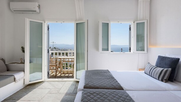A bedroom with a bed, a sofa, a balcony with a table and chairs, and a view of the sea. - Phaedrus Living: Paros Cycladic Residences 7 (Piso Livadi)
