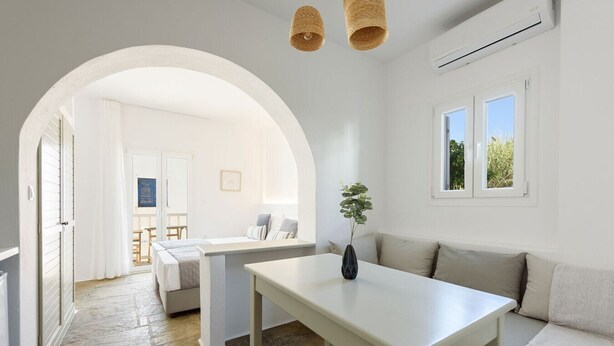 A modern, well-lit room with a white table, a sofa, and a large window. - Phaedrus Living: Paros Cycladic Residences 8 (Piso Livadi)