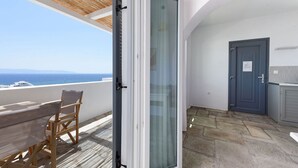 En balkon med udsigt over havet, en træstol, en glasdør og en blå dør.