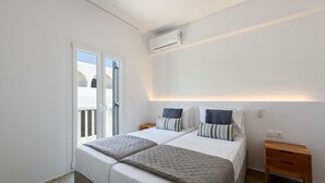 Et soveværelse med to senge, et vindue, en aircondition og et trænatbord.