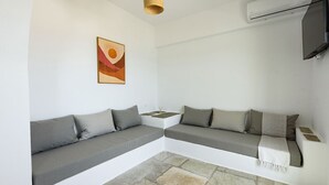Et moderne, minimalistisk værelse med en grå modulsofa, et lille sofabord, en vævet loftlampe og et vægmonteret fladskærms-TV.