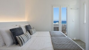 A bedroom with a bed, pillows, and a view of the sea through a glass door. - Phaedrus Living: Paros Cycladic Residences 11 (Piso Livadi)
