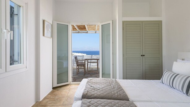 A bedroom with a bed, a view of the sea, and a door leading to a balcony. - Phaedrus Living: Paros Cycladic Residences 5 (Piso Livadi)