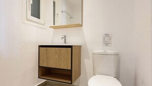 Une petite salle de bain avec des toilettes blanches, un meuble en bois et un miroir au-dessus du lavabo.