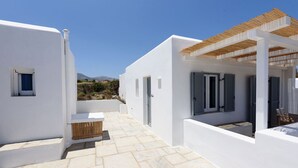 Un bâtiment blanc doté d’un patio carrelé, d’un banc en bois et d’une pergola.